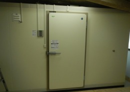 神奈川県伊勢原市の惣菜店バックヤードに新設したプレハブ冷蔵庫の外観。高断熱パネルと気密性の高い専用ドアを備え、衛生管理と保冷力を両立。